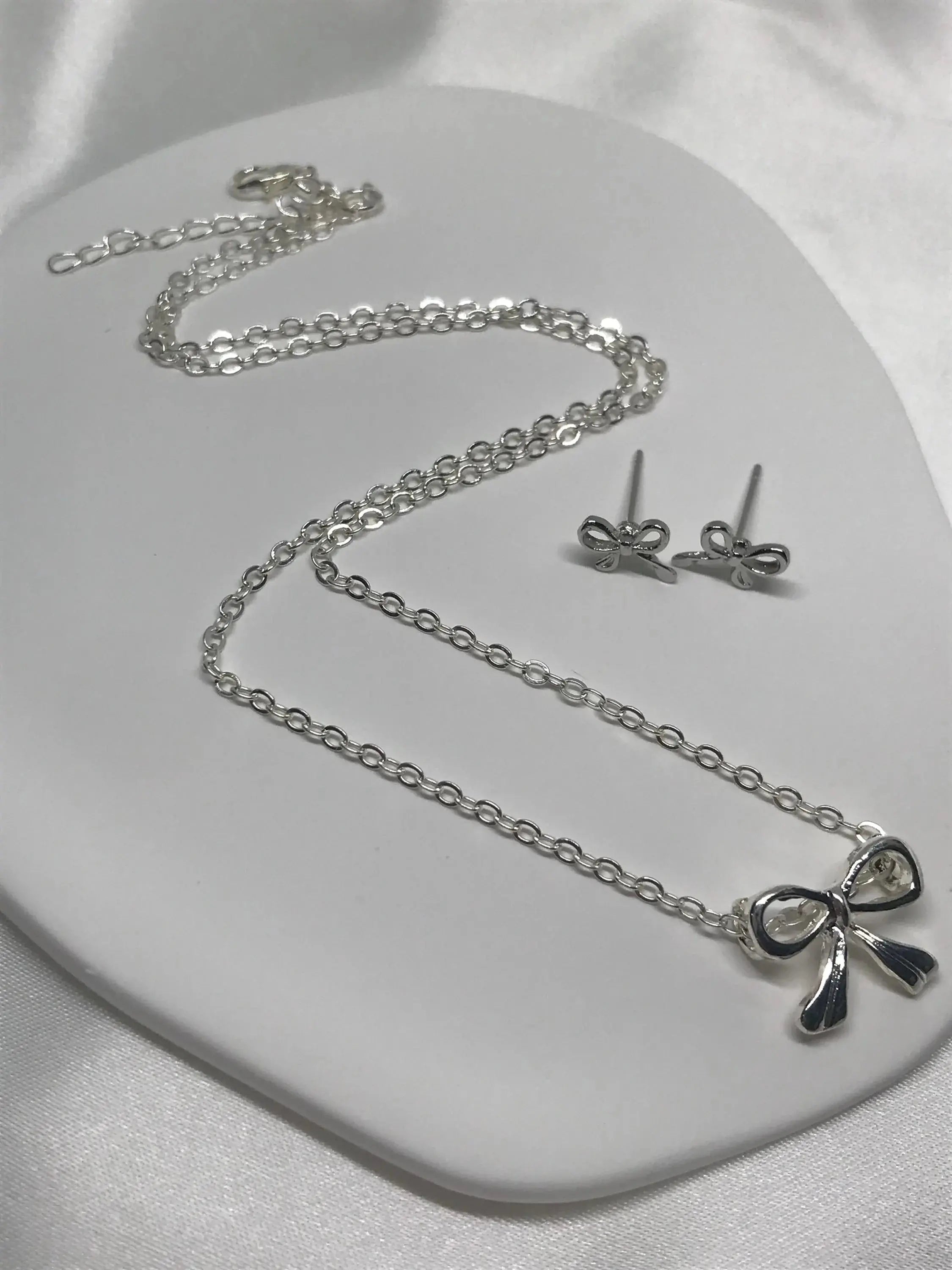 Silver necklace and earrings with bow details on a white surface